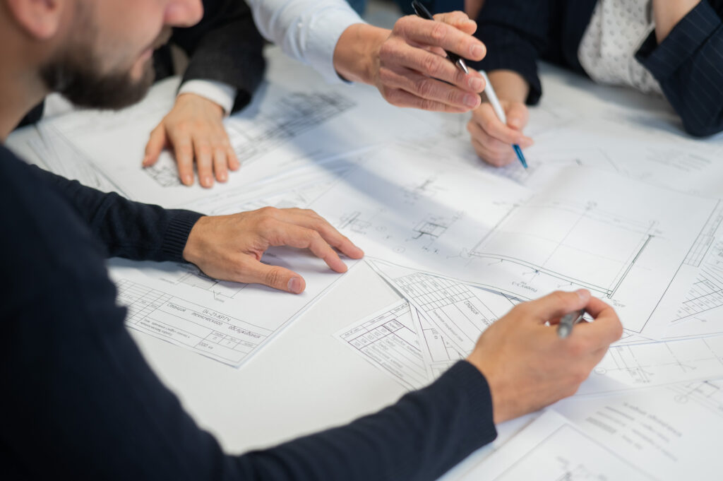 Groupe d’ingénieurs analysant des plans techniques autour d’une table lors d’une réunion de coordination.